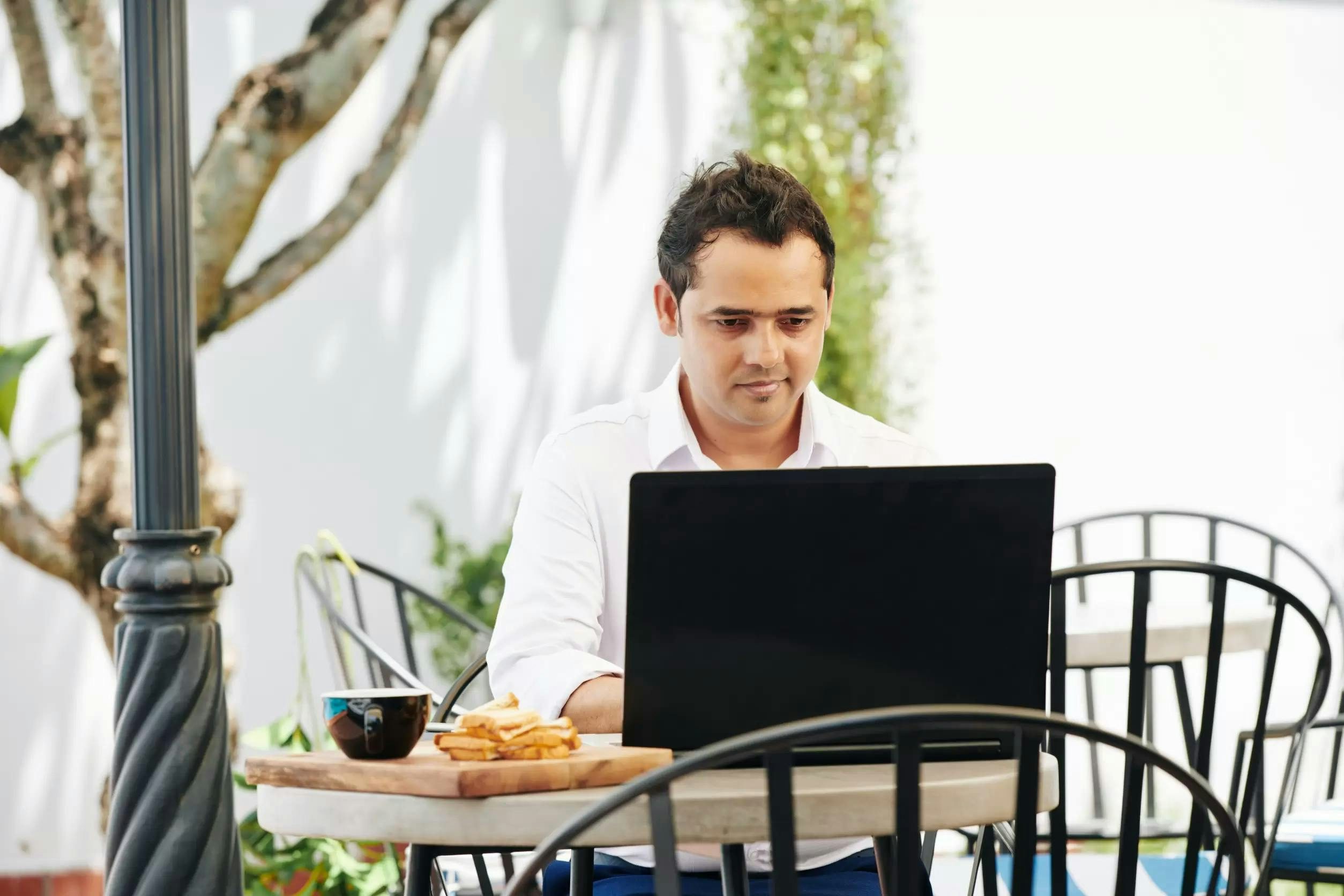 Man working outdoors in a cafe with a laptop and a plate of churros with chocolate