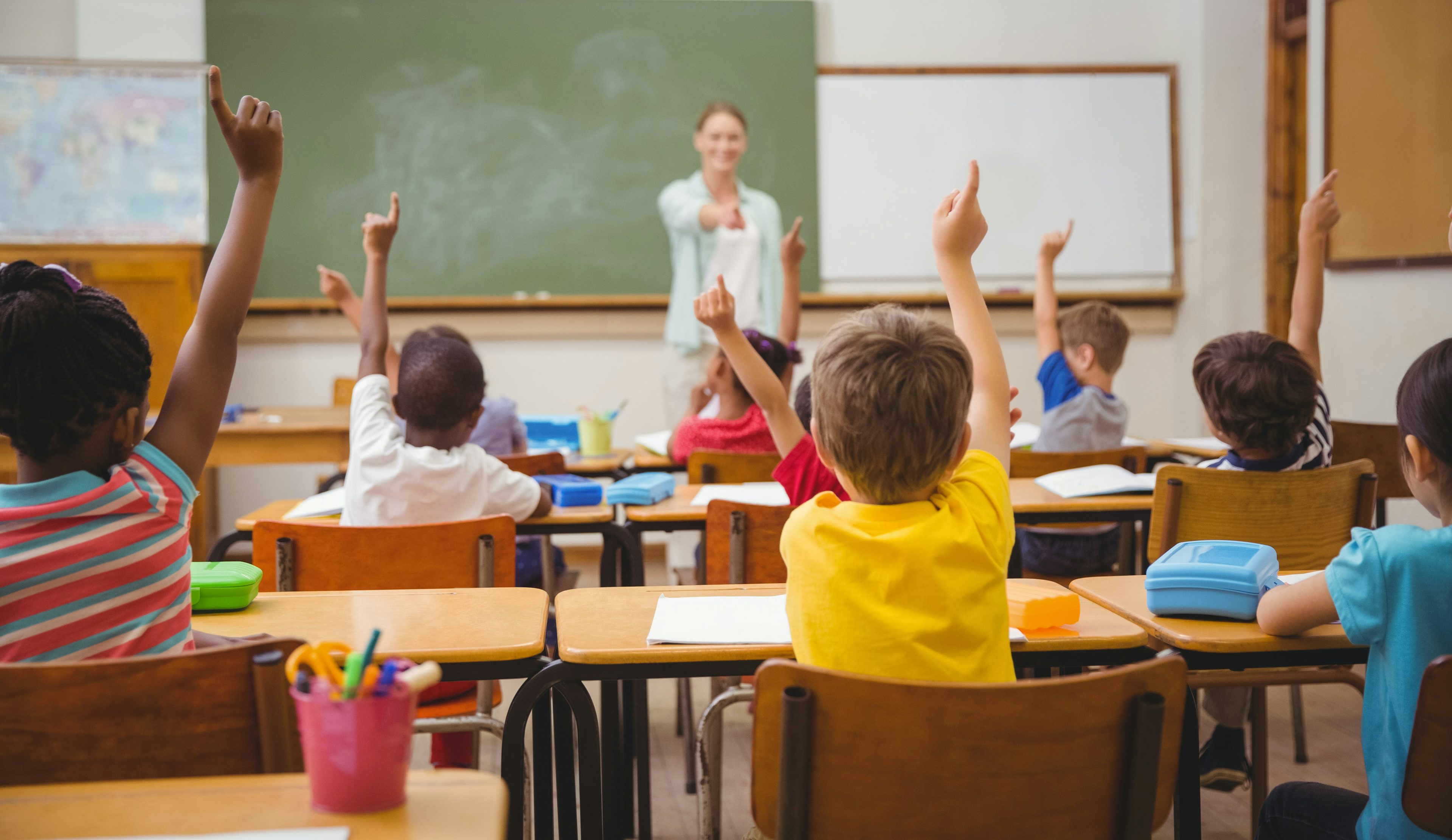 Children at their school desks raising their hands