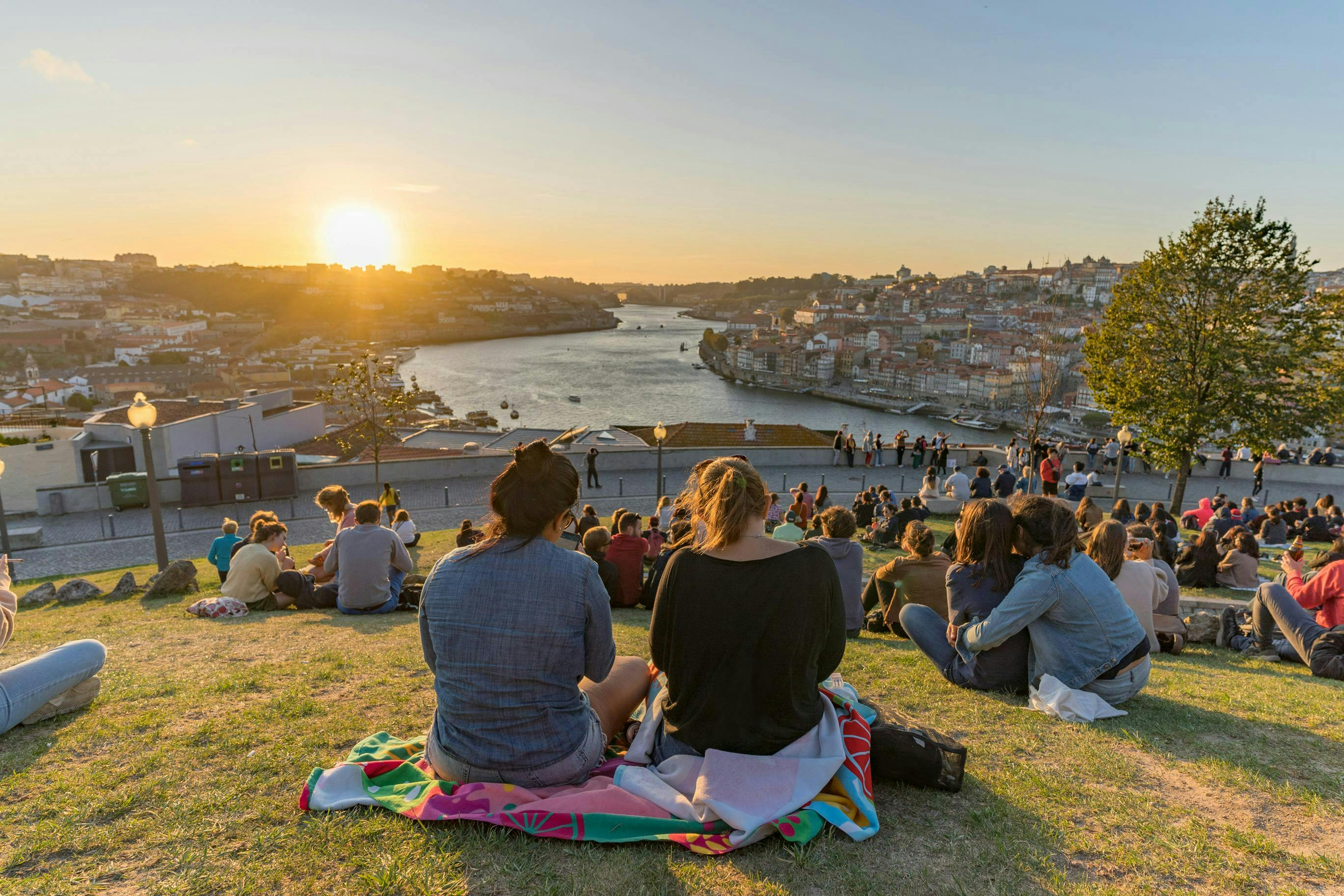 People sitting on a hill overlooking a river watching the sun set
